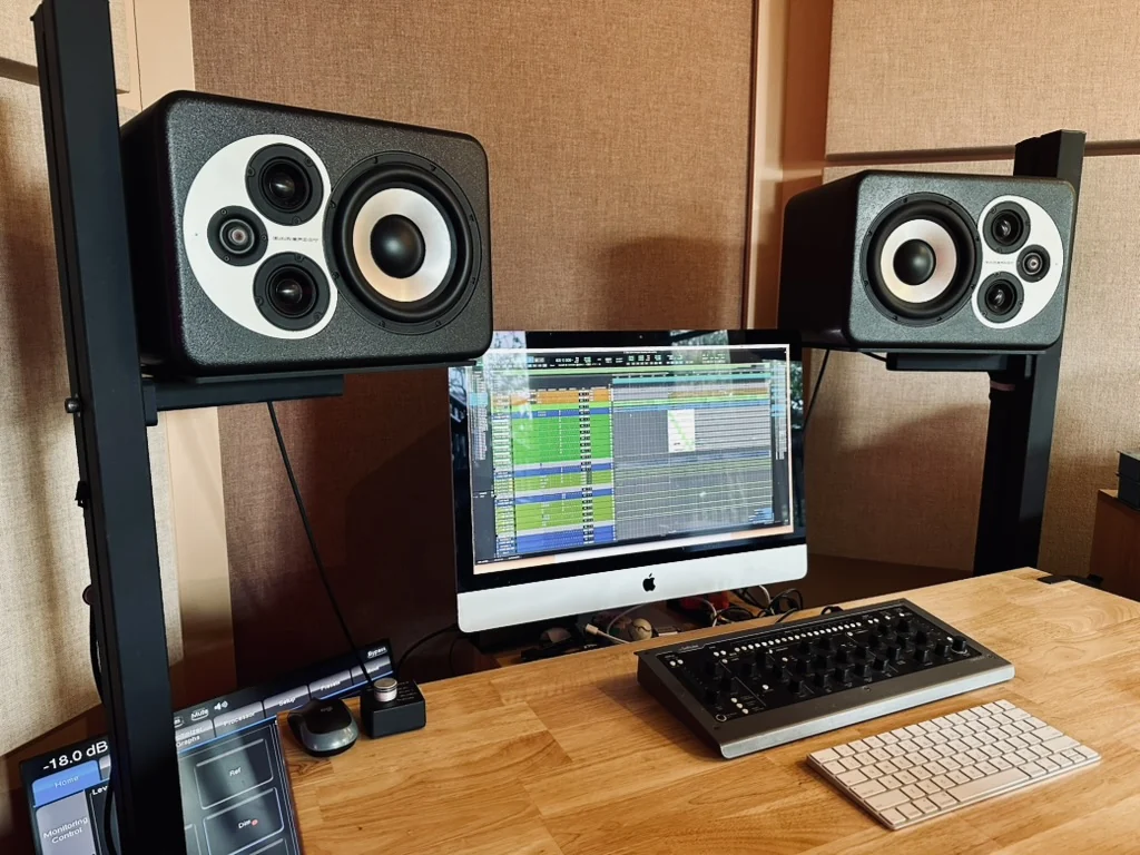 The studio: monitors on stands either side of a screen carrying a large multitrack session, with a control surface and monitor controller on the desk.